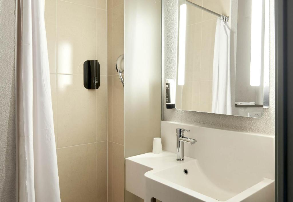 a white bathroom with a sink and a mirror at B&B HOTEL Paris Le Bourget in Le Bourget