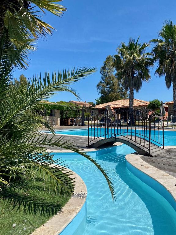 un pont sur une piscine bordée de palmiers dans l'établissement Résidence Dolce Vita de Palombaggia, à Porto-Vecchio