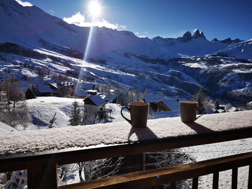 2 tasses à café assises sur un balcon avec une montagne enneigée dans l'établissement Appartement refait à neuf pour 8 personnes à Albiez-Montrond, à Albiez-Montrond