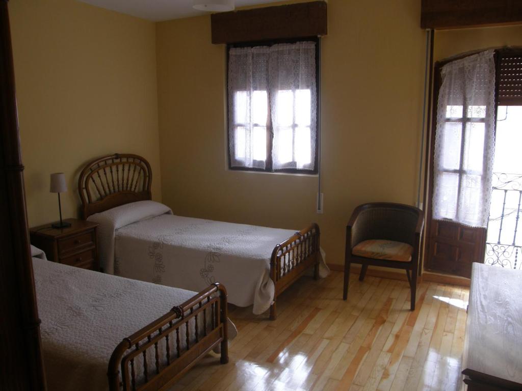sypialnia z 2 łóżkami i krzesłem oraz 2 oknami w obiekcie Casa Rural Baco w mieście Baños de Valdearados