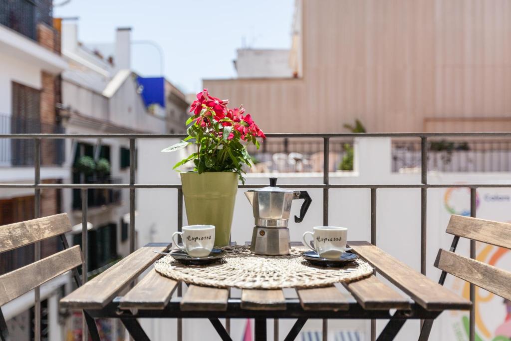 a wooden table with two cups and a vase with flowers at Nova Apartment by Hello Homes Sitges in Sitges