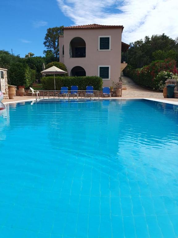 a large blue swimming pool with a house in the background at Emily's Apartments in Kassiopi