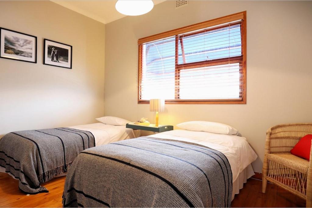 two beds in a room with a window and a chair at Cape Town cottage near colony of penguins in Simonʼs Town
