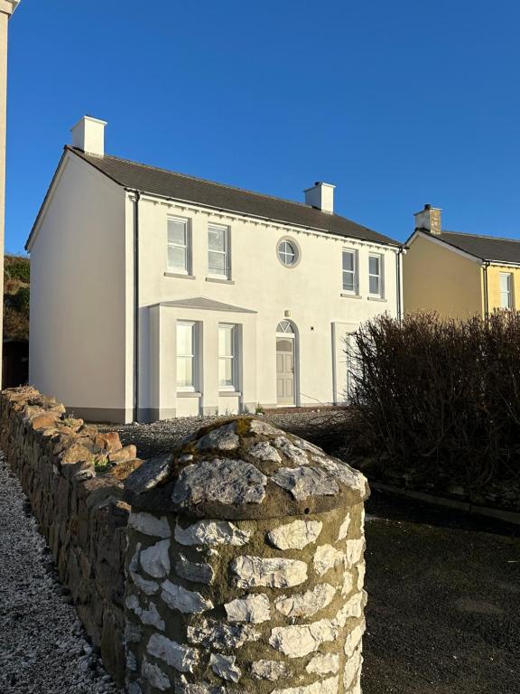 a white house with a stone wall in front of it at Church Bay House Rathlin in Rathlin Island