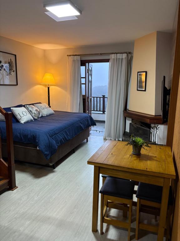 a bedroom with a bed and a table and a balcony at Apartamento no Home Green Home - Vista para a montanha in Campos do Jordão