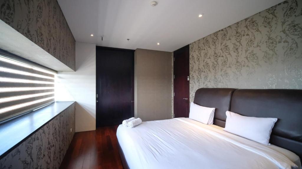 a bedroom with a white bed with a black headboard at Spacious and Restful 2BR at Sumatra36 Apartment By Travelio in Surabaya