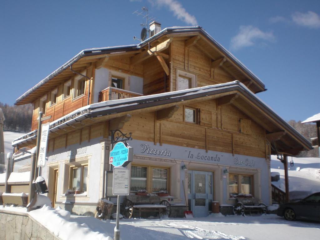 a log building in the snow with a sign in front at La Locanda in Livigno