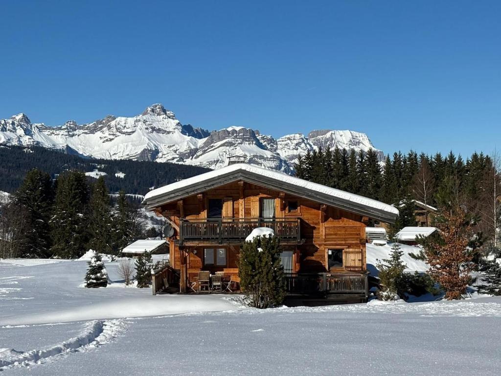 una baita di tronchi nella neve con montagne sullo sfondo di Chalet La Pioleute Megève a Megève