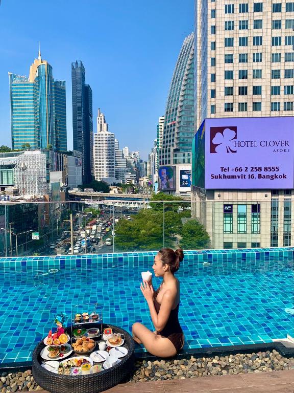 a woman sitting next to a pool with a tray of food at Hotel Clover Asoke - SHA Extra Plus in Bangkok