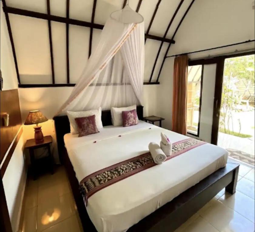 a bedroom with a large white bed with a window at Nelly Homestay Bungalows Gili Air in Gili Air