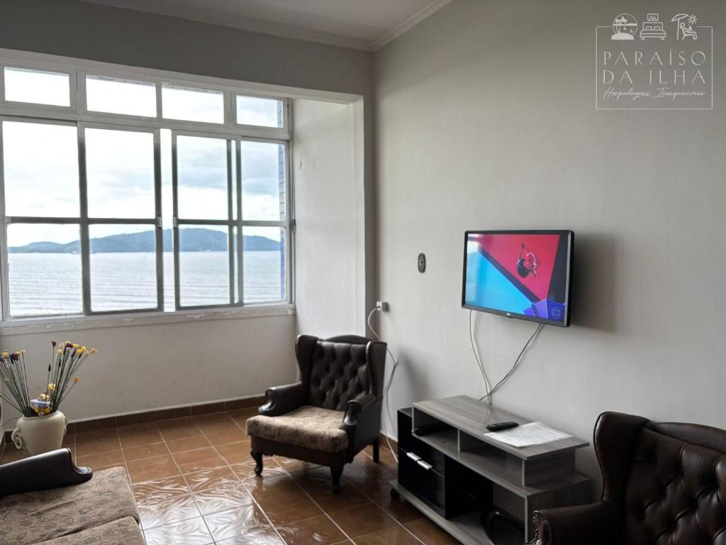 ein Wohnzimmer mit Fernseher und Sessel in der Unterkunft Apartamento Frente Mar Vista Panorâmica Incrível in São Vicente