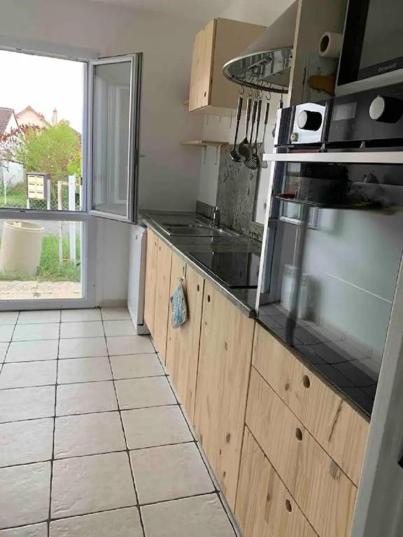 une cuisine avec des placards en bois et une grande fenêtre dans l'établissement jolie maison lumineuse à La Roche Posay, à La Roche-Posay