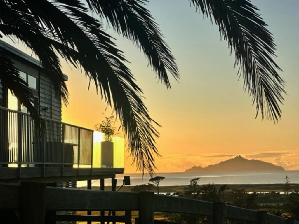 a sunset view of the ocean and a building at The Chocolate Box - Waipu Cove Holiday Home in Waipu