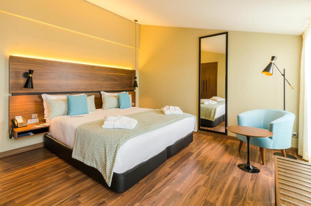 A warmly lit bedroom with a king-size-looking bed, full-height mirror and window-side chair.