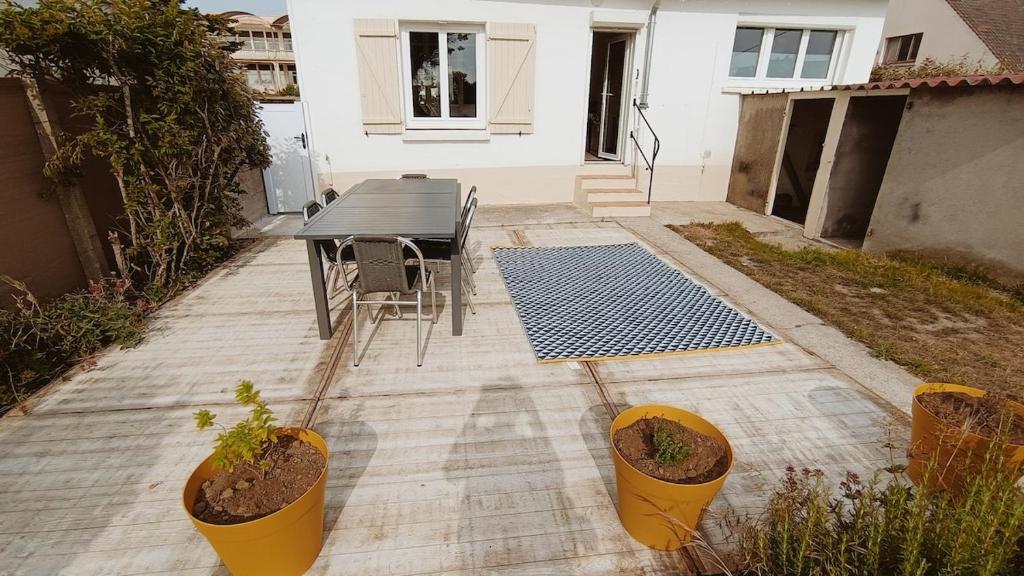 un patio avec une table, des chaises et des plantes en pot dans l'établissement Agréable maison avec jardin à 100m de la plage, à Berck-sur-Mer