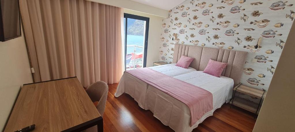 a bedroom with a bed with pink pillows and a table at Casa Linda Baía in Porto da Cruz
