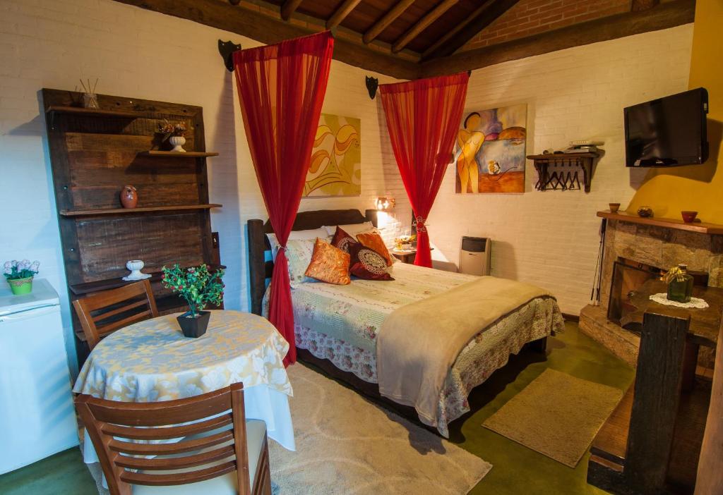 a bedroom with a bed and a table and a television at Pousada Alto da Neblina in Monte Verde