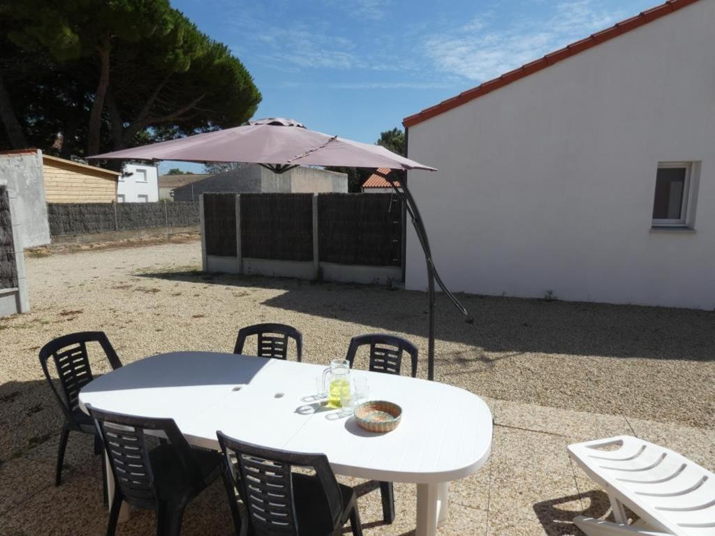 une table blanche avec des chaises et un parasol dans l'établissement Maison conviviale à 500m de la plage, animaux admis, terrasse et WiFi - FR-1-540-307, à Notre-Dame-de-Monts