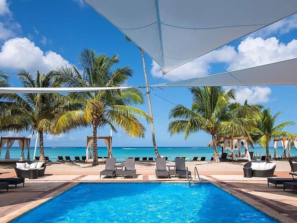 a swimming pool next to a beach with palm trees at Lovely apartment by the Caribbean in Bayahibe
