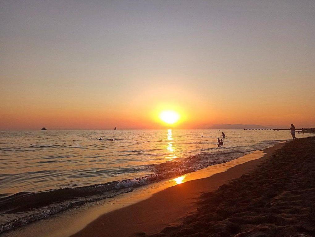 a sunset on the beach with people in the water at Perla Azzurra - Forte dei Marmi - Cinque Terre in Montignoso