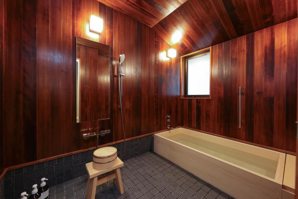 a bathroom with wooden walls and a tub and a stool at Tsukihitei in Nara