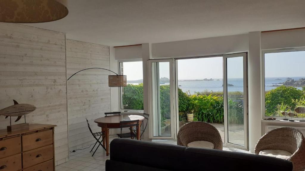 - un salon avec un canapé, une table et des fenêtres dans l'établissement Un vrai paradis avec terrasse face à la mer, à Plougasnou
