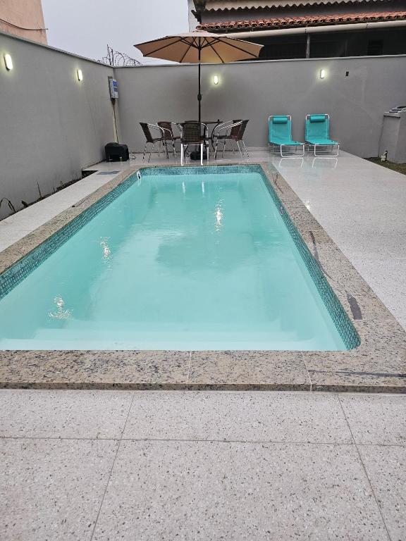 a large blue swimming pool with chairs and an umbrella at Casa de Praia Castanheiras in Guriri