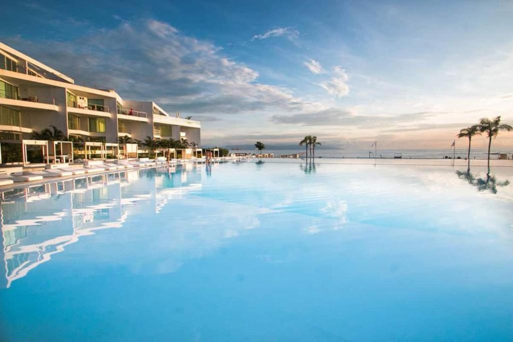 a large swimming pool next to a beach with palm trees at Aria Ocean Beachfront Condos in Nuevo Vallarta