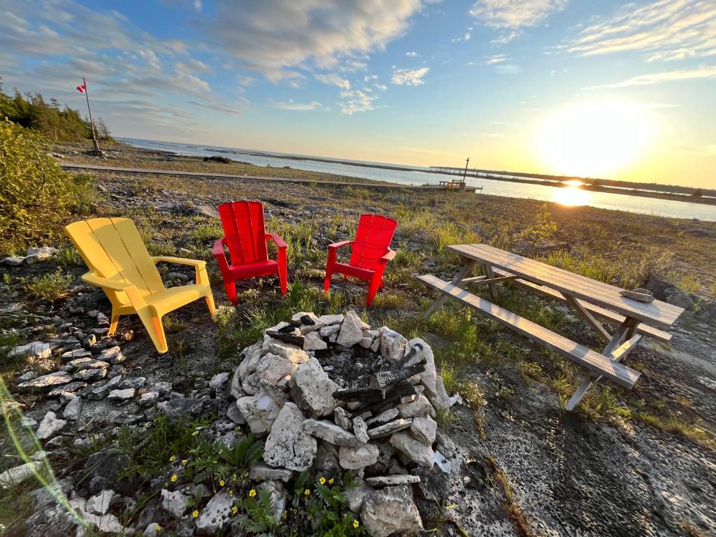 three chairs and a picnic table next to a fire pit at Silver Birch Waterfront Sunsets Tobermory in Tobermory