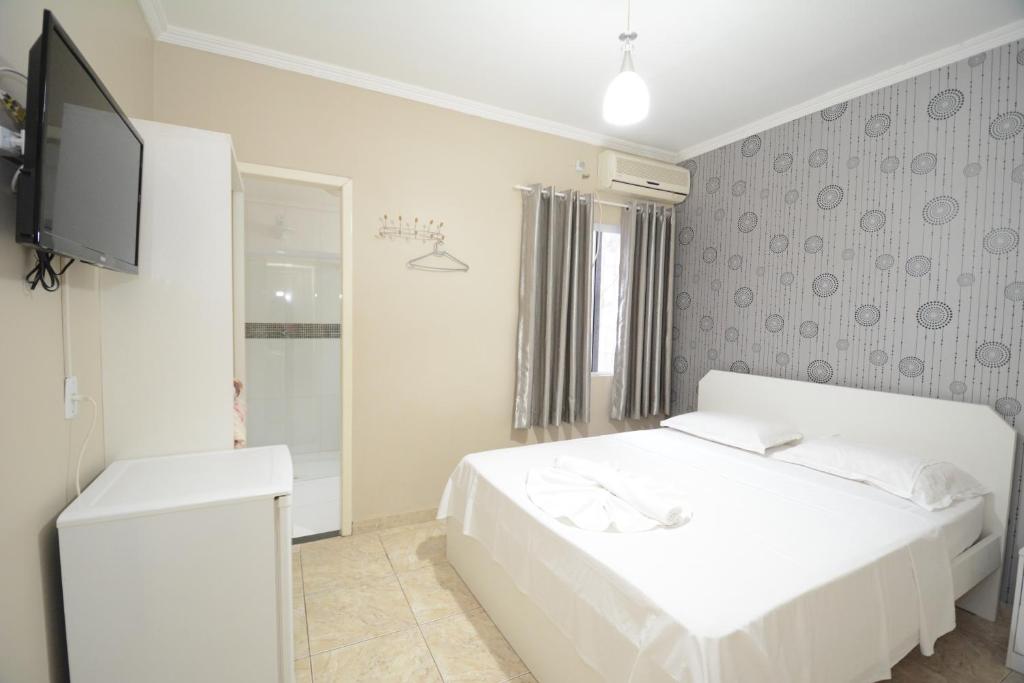 a white bedroom with a white bed and a television at Pousada Quedas D'água in Foz do Iguaçu