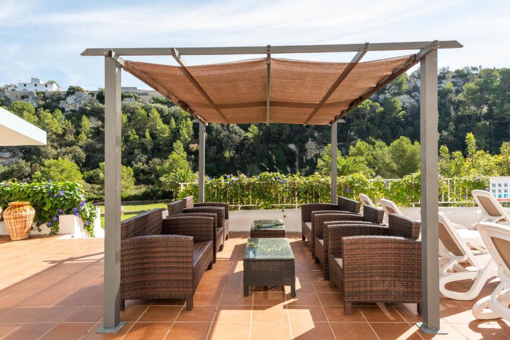 an outdoor patio with wicker chairs and a canopy at Apartamentos alta galdana playa in Cala Galdana