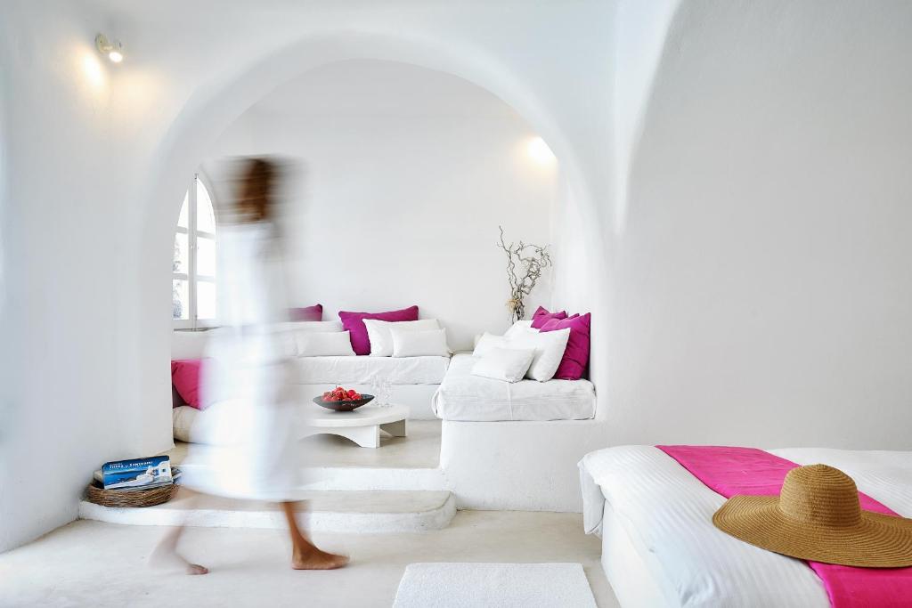 a woman walking through a living room with white furniture at Finikia Memories Hotel in Oia
