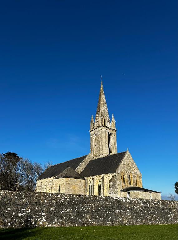 an old church with a steeple behind a stone wall at Little Omaha in Vierville-sur-Mer