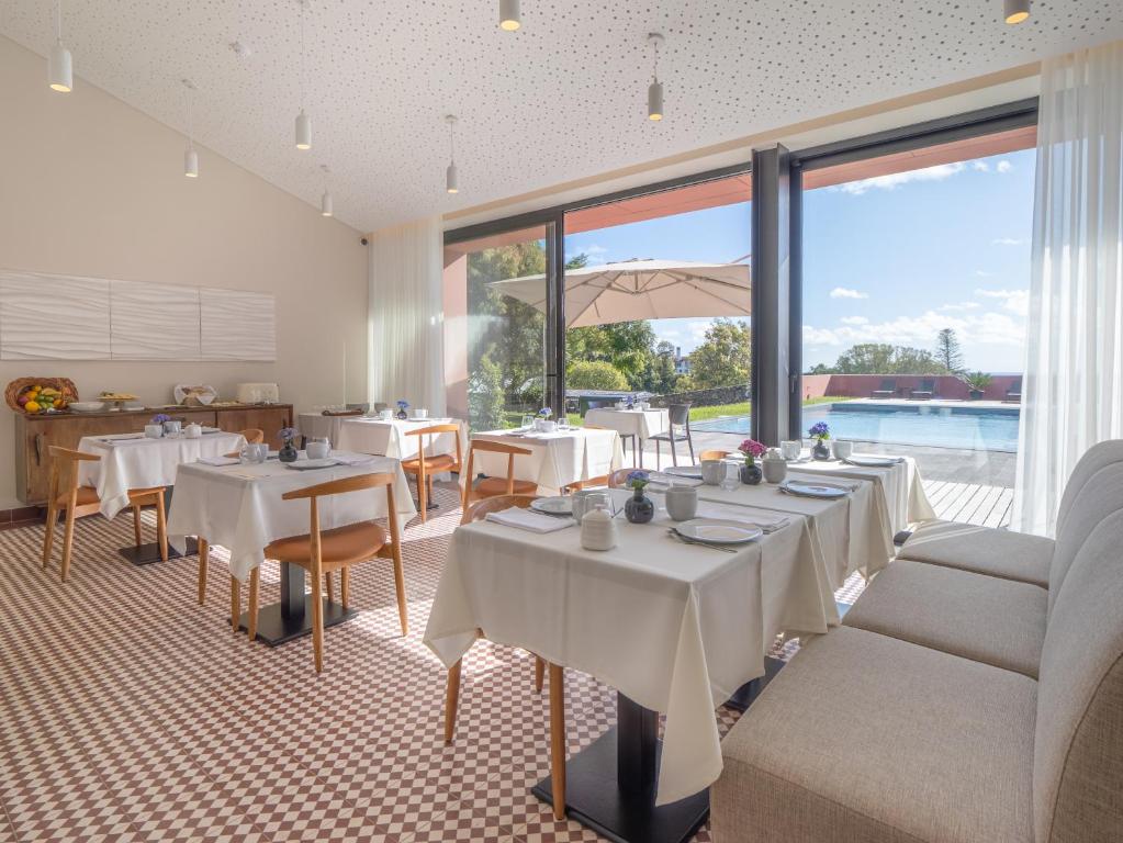 a restaurant with white tables and chairs and windows at Quinta da Casa Grande in Ponta Delgada