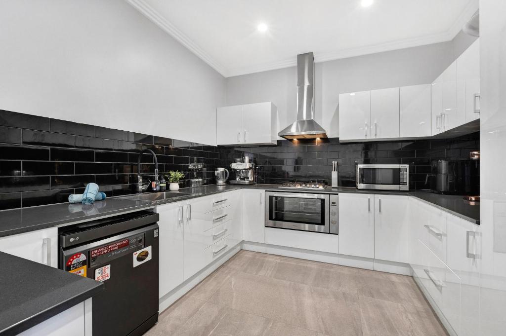 a kitchen with white cabinets and black appliances at Bassendean Bliss By Swan Bnb Management in Perth