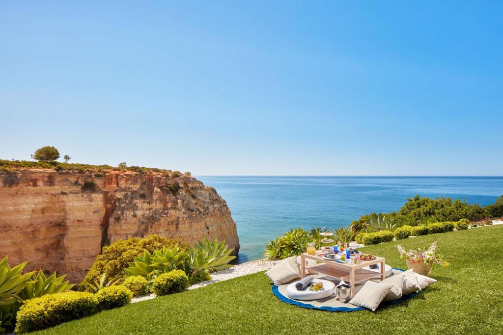 a table and chairs on the grass near the ocean at Tivoli Carvoeiro in Carvoeiro