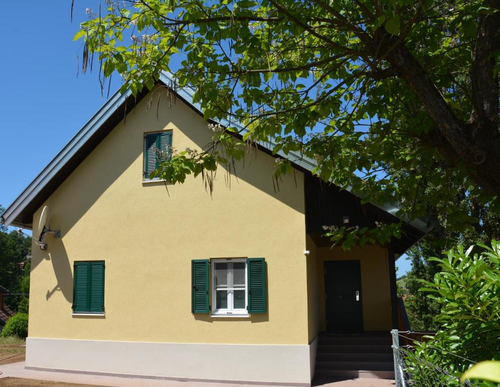 a yellow house with green shutters and a tree at Ferienhaus Moor-Rosl in Gamlitz