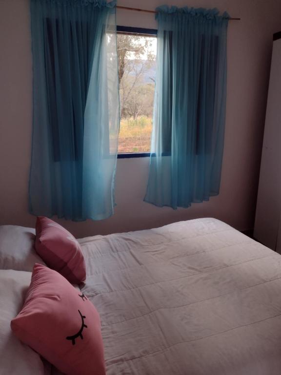 a bedroom with a bed with blue curtains and a window at Achô na Roça STL in São Thomé das Letras