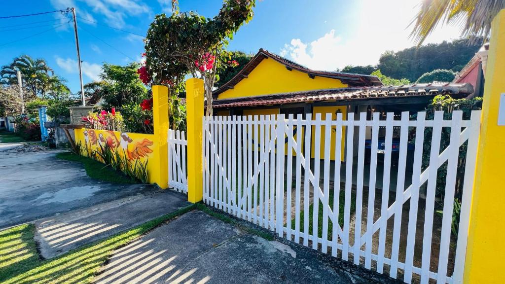 a white fence in front of a yellow house at Casa Bem-te-vi - Passarim Hospedagem in Cumuruxatiba