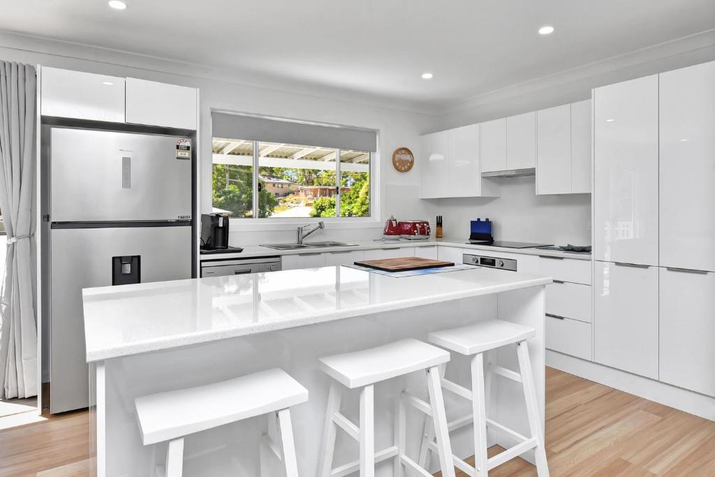 a white kitchen with white cabinets and a large island at Gidget's Getaway in Nelson Bay