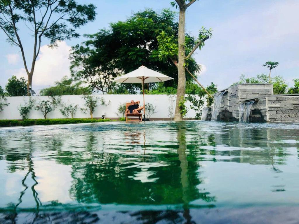 eine Person, die unter einem Regenschirm neben einem Pool sitzt in der Unterkunft Rose Villa Thai Nguyen - Venuestay in Thượng Nhân