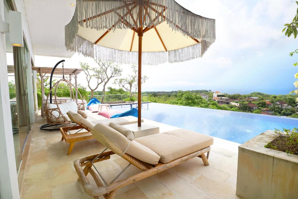a patio with chairs and an umbrella and a pool at Villa Aventus Uluwatu in Uluwatu