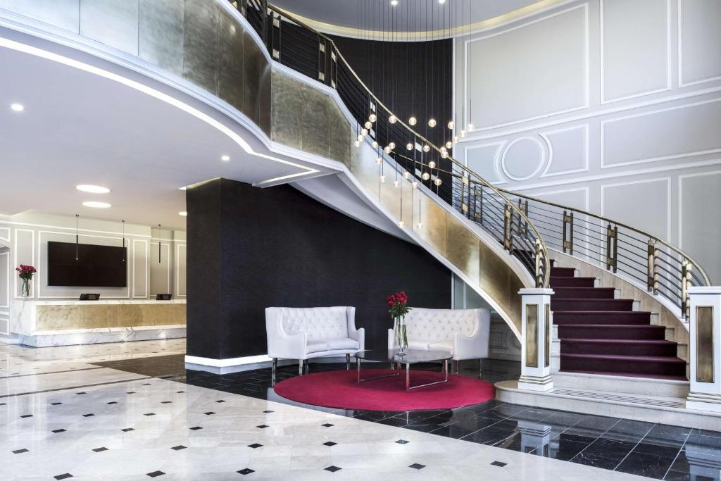 a lobby with a staircase with two chairs and a table at NH Collection Plaza Santiago in Santiago