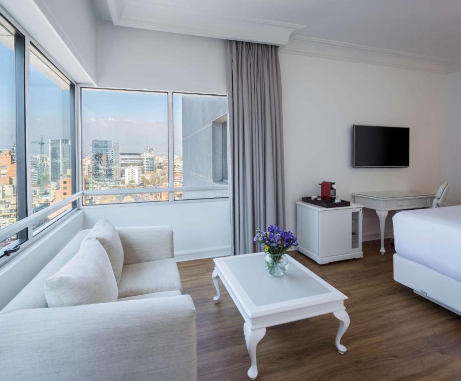 a living room with a white couch and a large window at NH Collection Plaza Santiago in Santiago