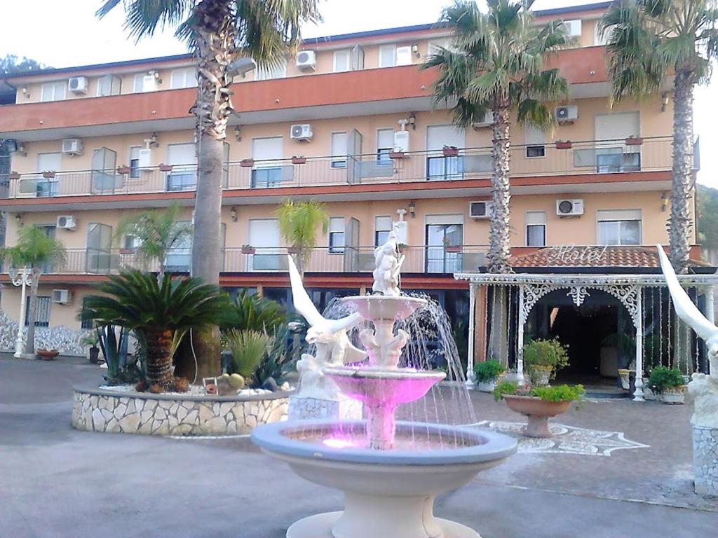 une fontaine en face d'un grand bâtiment avec des palmiers dans l'établissement Hotel Happy Days, à Licola