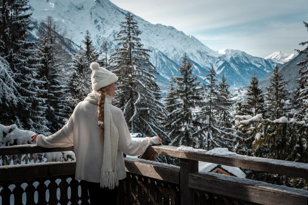a woman standing on a balcony overlooking a snowy mountains at Hôtel Les Chalets de Philippe avec Jacuzzis Privatifs in Chamonix-Mont-Blanc