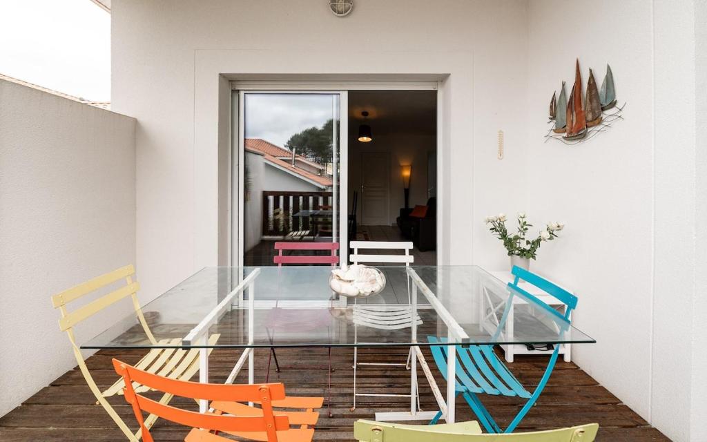 une table à manger en verre avec des chaises colorées dans l'établissement Maison de vacances Navarrosse, à Biscarrosse