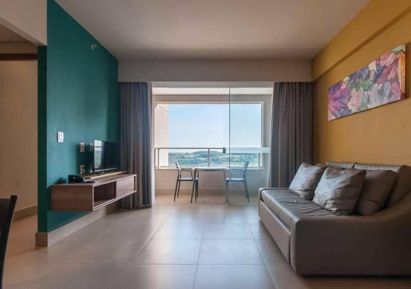 a living room with a couch and a large window at Apartamento Enjoy Solar das Águas Park Resort in Olímpia