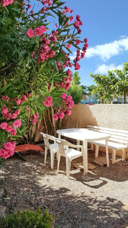 deux bancs blancs et une table et des fleurs roses dans l'établissement Appartement cosy à Port Leucate 44 m² avec terrasse et jardin, à Port-Leucate