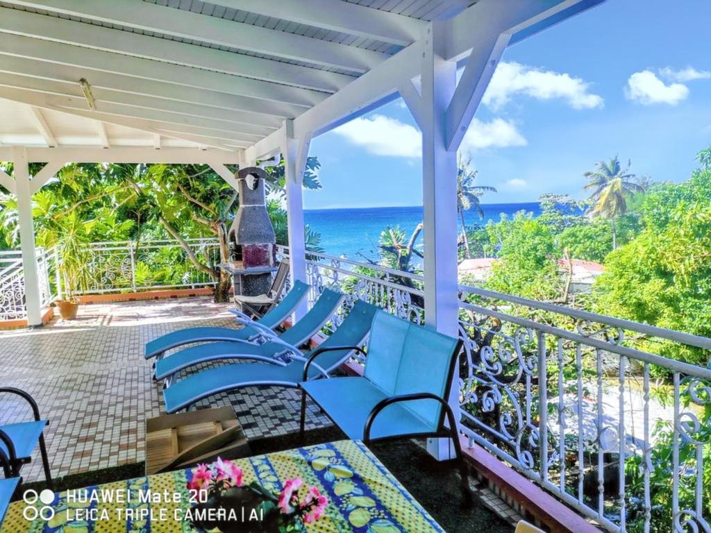 Appartement confortable avec vue sur mer à Deshaies, 48 m² في ديساي: شرفة بمقاعد زرقاء والمحيط في الخلفية